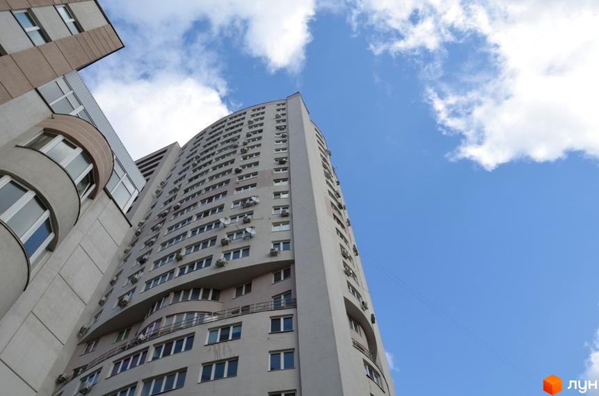 Фасад Житлового комплексу Вікторія: високий світлий будинок з вигнутими лініями, численними вікнами та зовнішніми блоками кондиціонерів.