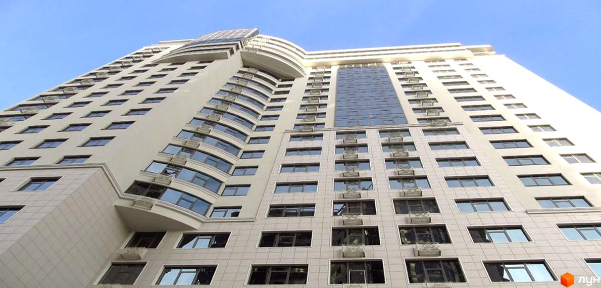 Житловий комплекс Перша Перлина з сучасним фасадом та великими вікнами. Прибудинкова територія озеленена та облаштована для відпочинку.