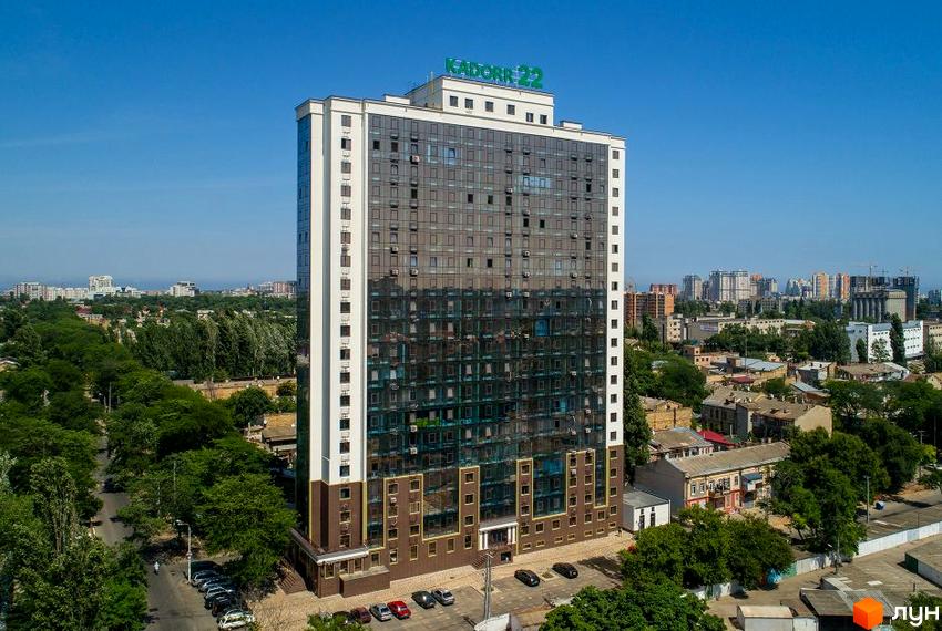 Висотна новобудова KADORR 22 з панорамним склінням та білими фасадами. Навколо будинку зелені насадження та міський пейзаж.