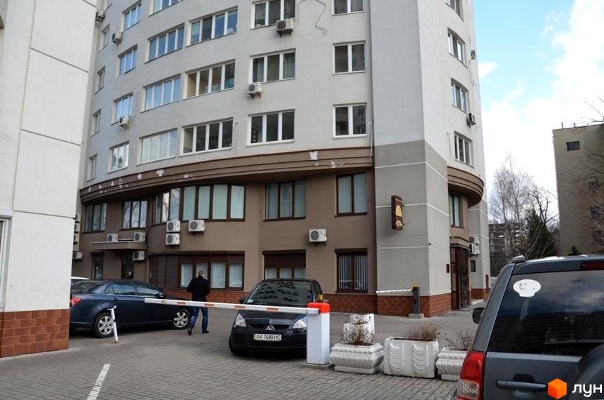 Житловий комплекс Вікторія: багатоповерховий будинок світло-сірого та коричневого кольорів з численними вікнами. Прибудинкова територія має шлагбаум та бруківку.