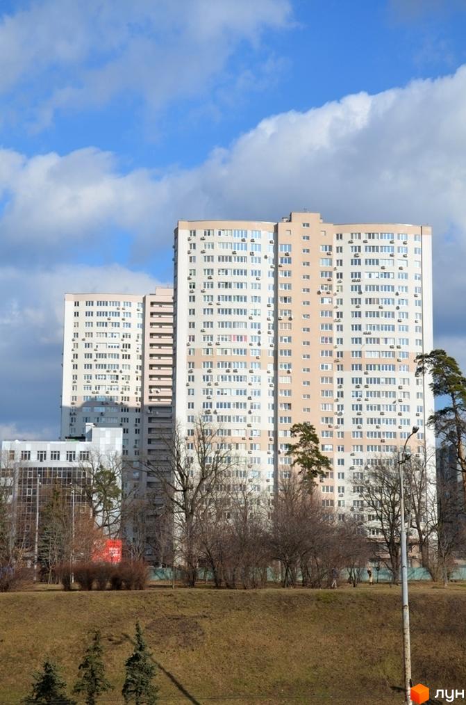 Житловий комплекс Вікторія: високі будинки зі світлими фасадами та численними вікнами. Перед комплексом розташовані дерева без листя та зелений пагорб.