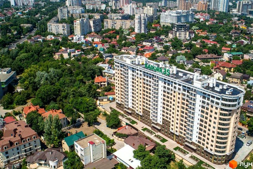 Вид на житловий комплекс Тридцять п'ята перлина з фасадом світло-бежевого кольору та зеленим написом на даху. Навколо розташовані дерева та інші будівлі.