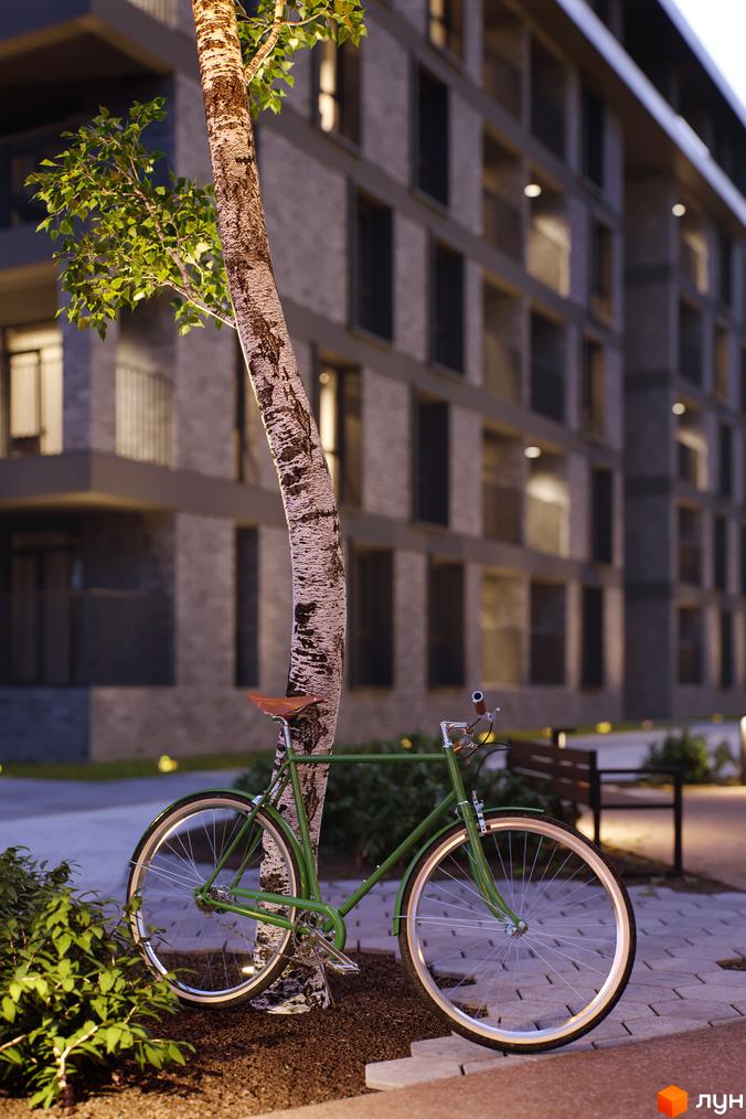 Зелений велосипед біля дерева на фоні багатоквартирного будинку ЖК Avalon Time. Прибудинкова територія з лавкою та освітленням.
