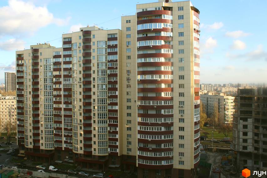 Багатоповерхові будинки Житлового комплексу Парковий з бежевим фасадом та коричневими балконами. Навколо видно дерева, дорогу з автомобілями та інші міські забудови.