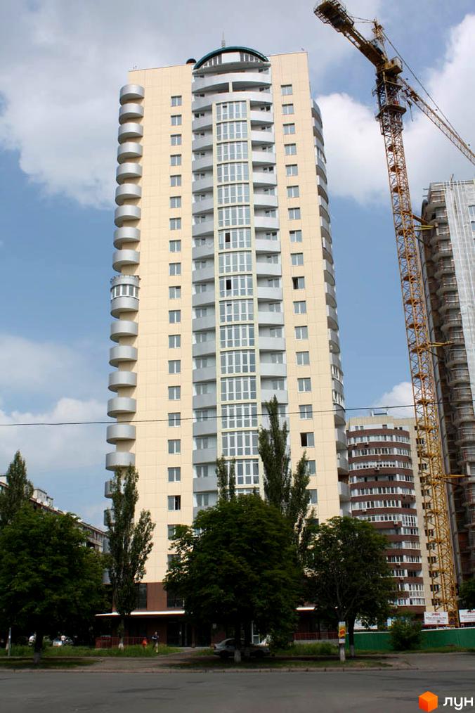 Житловий комплекс Парковий: високий будинок світлого кольору з численними вікнами та округлими балконами, оточений деревами та будівельним краном.