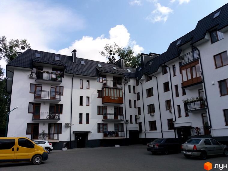 Зовнішній вигляд новобудови на вул. Авіаційна, 2а з прибудинковою територією та автомобілями.