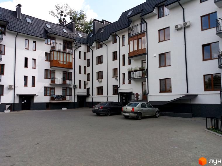 Зовнішній вигляд новобудови на вул. Авіаційна, 2а, з прибудинковою територією та автомобілями на парковці.