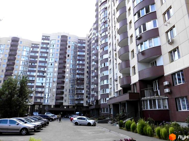 Багатоповерхові будинки житлового комплексу Парковий світло-бежевого та темно-коричневого кольорів з балконами. Перед будинками є паркінг та озеленена територія.