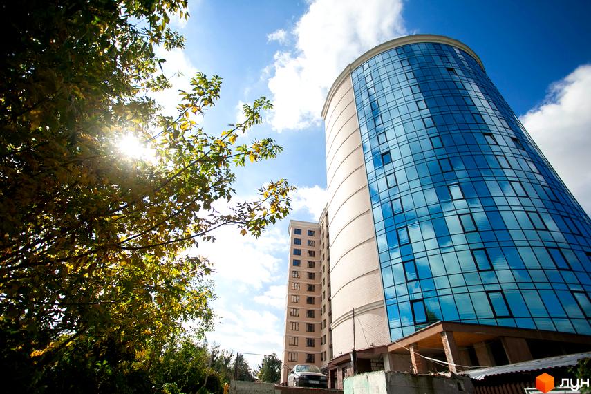 Зображення сторінки Житлового комплексу Paradise. Вигляд на круглий будинок з синіми вікнами та частково скляним фасадом.