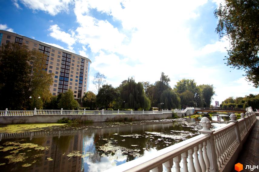 Багатоповерховий житловий комплекс Paradise з вигнутим фасадом та світлими стінами, розташований біля річки з набережною та зеленими деревами.