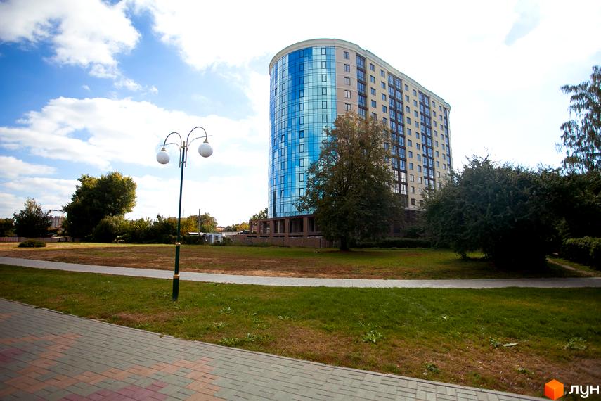 Багатоповерховий будинок Житлового комплексу Paradise з вигнутим скляним фасадом та численними вікнами. Навколо будинку зелені насадження та доріжки.