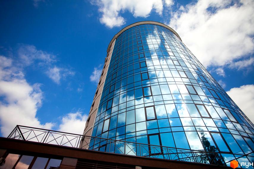 Зображення фасаду будівлі Житлового комплексу Paradise з панорамними вікнами, в яких відбивається блакитне небо з хмарами. Вигляд знизу вгору.