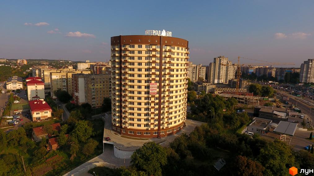 Вид з висоти пташиного польоту на багатоповерхівку на вулиці Бережанській, 54. Кругла будівля з великою кількістю вікон та коричневими вставками.