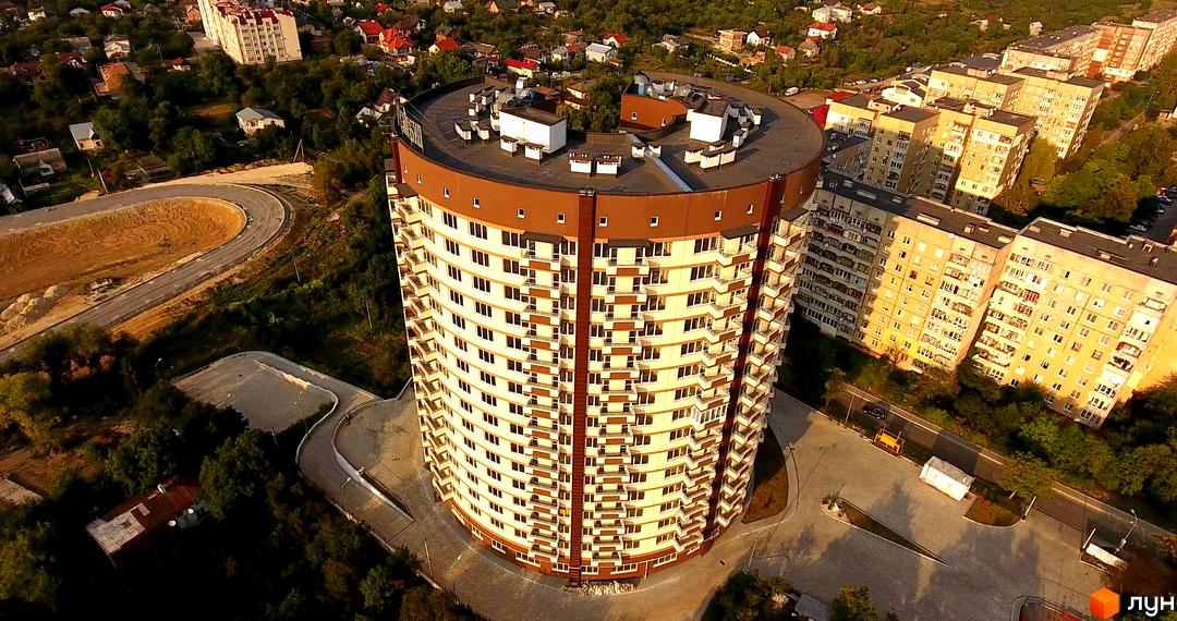 Зображення житлового комплексу на вулиці Бережанська, 54. Вид з висоти пташиного польоту на круглий багатоповерховий будинок та прибудинкову територію.