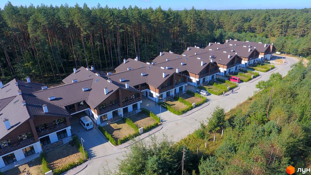 Котеджне містечко Bruhsell: сучасні будинки з коричневими дахами та білими стінами, розташовані серед зелених насаджень та соснового лісу. Прибудинкова територія з доглянутими газонами та доріжками.