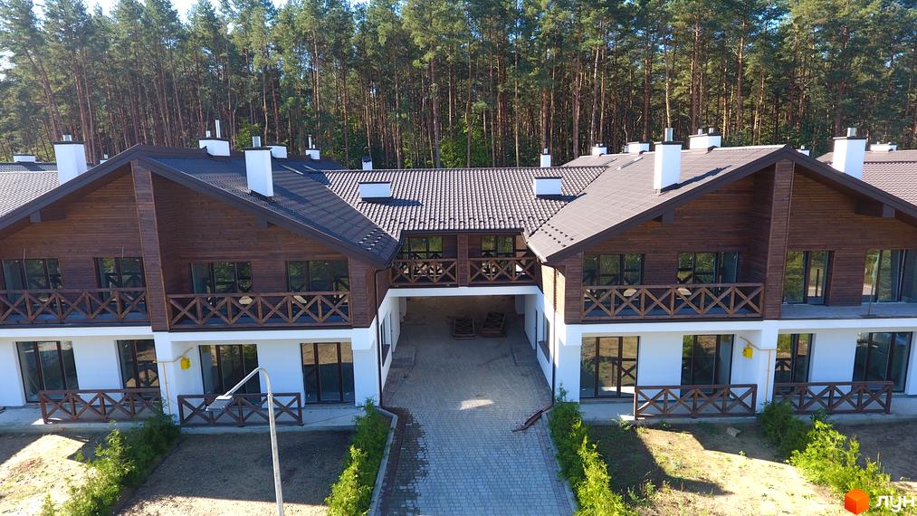 Котеджне містечко Bruhsell. Двоповерхові будинки з дерев'яними фасадами та темними дахами на тлі лісу. Дорога веде до центрального проїзду.