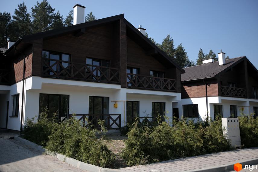 Двоповерхові будинки Котеджного містечка Bruhsell з білими фасадами, темним дерев'яним оздобленням та балконами. Перед будинками висаджені зелені кущі.