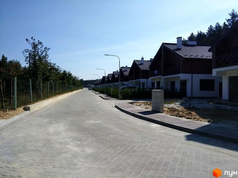 Котеджне містечко Bruhsell: ряд будинків з темними дахами, білими фасадами та дерев'яними балконами. Вулиця з бруківкою та зеленою огорожею.