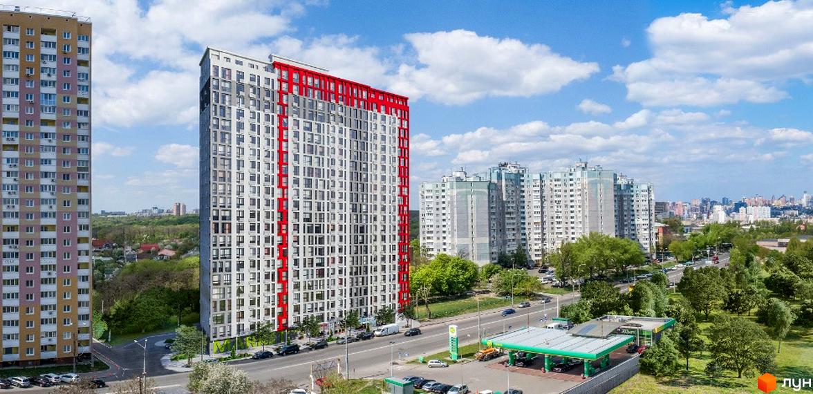 Зовнішній вигляд новобудови Науки 58 з червоними елементами на фасаді та прилегла територія з дорогою та газовою станцією.