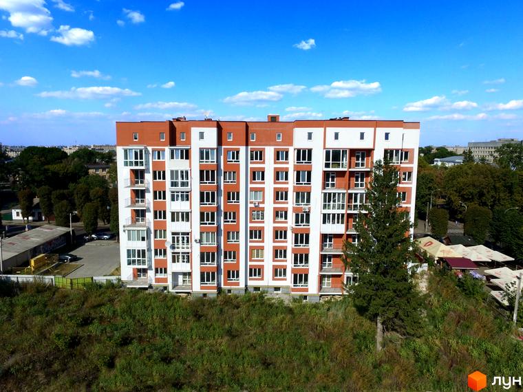 Висотна будівля ЖК Сіті Парк з білими та коричневими фасадами на тлі блакитного неба. Поруч зелені насадження та прибудинкова територія.