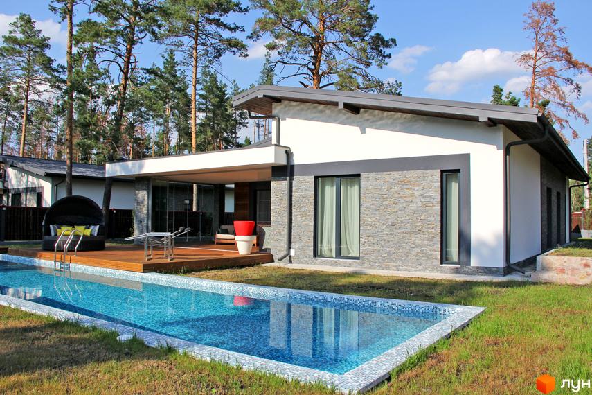 Будинок Котеджного містечка Хвойний квартал з білим фасадом та кам'яним облицюванням. На подвір'ї басейн, дерев'яна тераса та зелений газон.