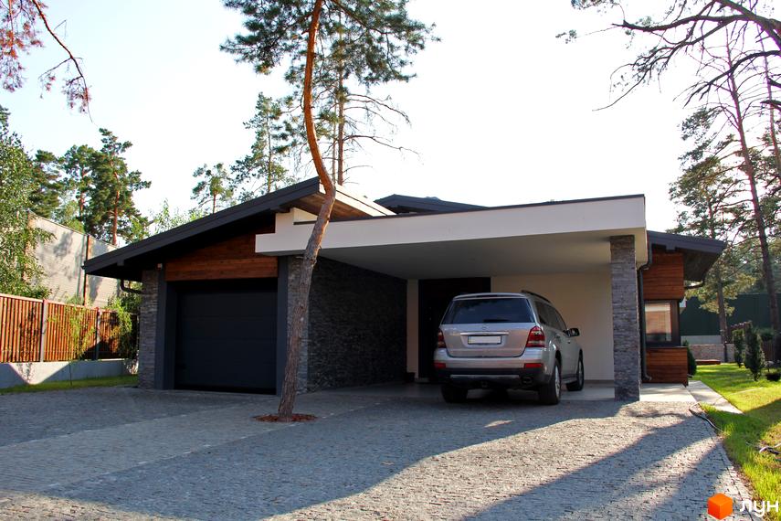 Котеджне містечко Хвойний квартал: будинок з темним дахом, дерев'яною обробкою та кам'яним облицюванням, з гаражем та навісом. Двір вимощений бруківкою.