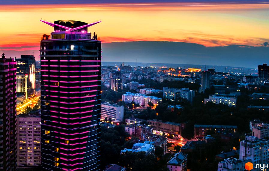 Житловий комплекс Jack House з рожевою підсвіткою на фоні вечірнього міста. Висотна будівля з оригінальною формою даху виглядає вражаюче на тлі міського пейзажу.
