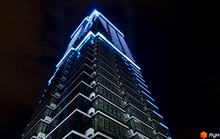 Нічна фотографія житлового комплексу Jack House з синьою підсвіткою фасаду. Будинок має скляні вікна та кондиціонери на кожному поверсі.