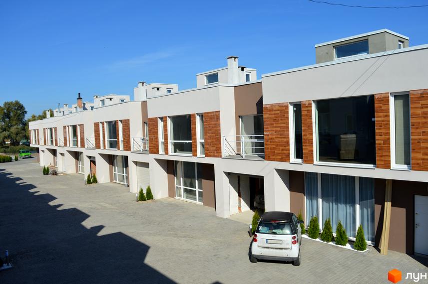 Таунхауси Belvedere City з великими вікнами та цегляним фасадом. Перед будинками розташований двір з бруківкою та невеликим паркуванням.