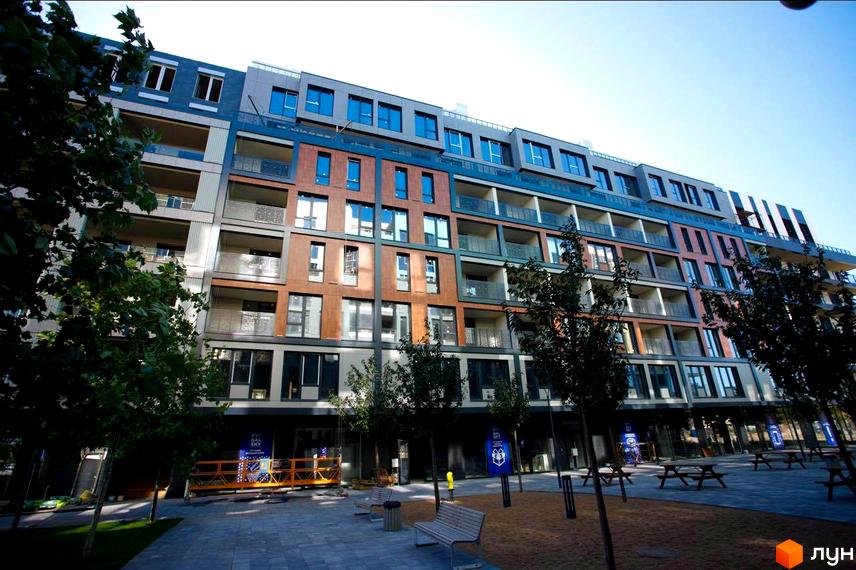 Багатоповерховий будинок Житлового району Rybalsky з фасадом у сірих, синіх та коричневих тонах. Прибудинкова територія має зелені насадження, лавки та пішохідні доріжки.