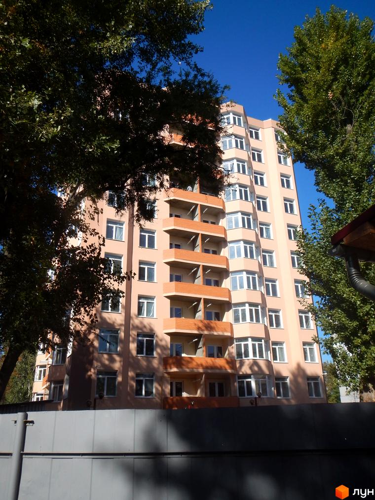 Зовнішній вигляд будинку ЖК Нове місто. Багатоповерховий будинок з балконами та вікнами на тлі блакитного неба та дерев.