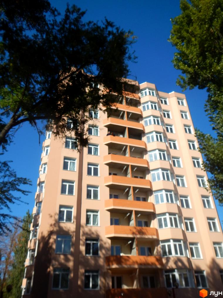 Зовнішній вигляд багатоповерхового будинку ЖК Нове місто з балконами та вікнами на фоні блакитного неба та дерев. Фото новобудови.