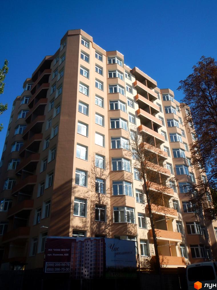 Житловий комплекс Нове місто - багатоповерховий будинок з балконами та великою кількістю вікон на фоні блакитного неба. На передньому плані видно частину рекламного банера.