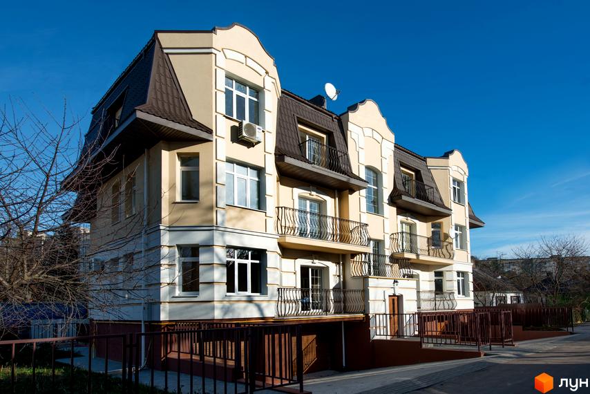 Зовнішній вигляд триповерхового будинку з балконами та мансардою на вул. Клима Савури, 8. Навколо будинку розташована прибудинкова територія з огорожею.