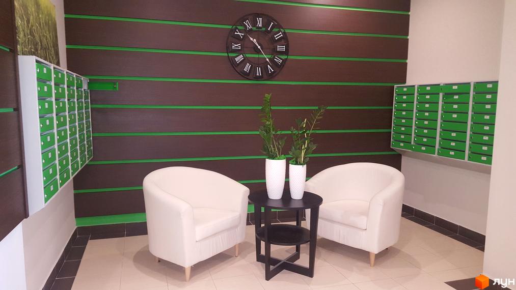 Інтер'єр холу в ЖК Solo Park. Стіни оздоблені панелями з декоративними вставками. У холі розміщені поштові скриньки, годинник, крісла та столик.