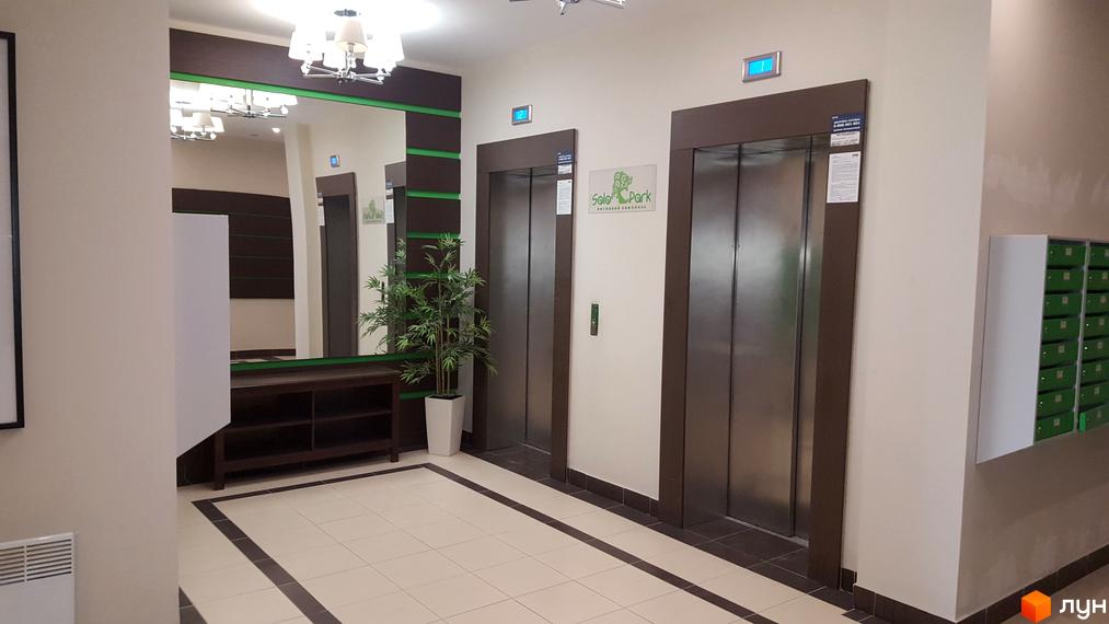 Холл житлового комплексу Solo Park з двома ліфтами. На стінах розташовані дзеркала та декоративні елементи. На підлозі плитка з візерунком.