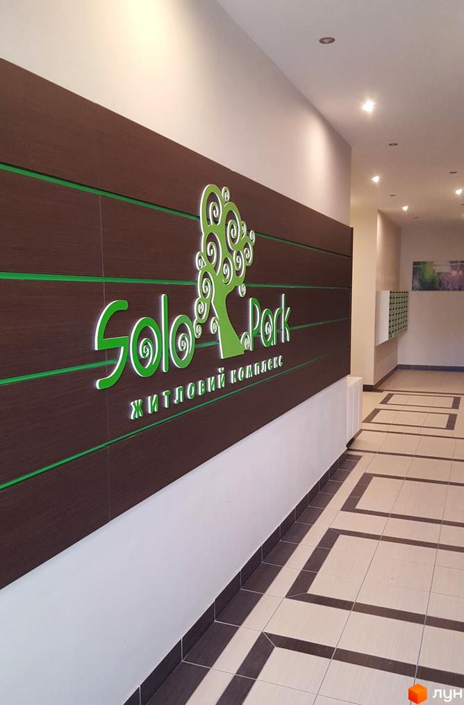Фасад ЖК Solo Park з вивіскою та логотипом у вигляді дерева. Коридор з плиткою на підлозі та поштовими скриньками.
