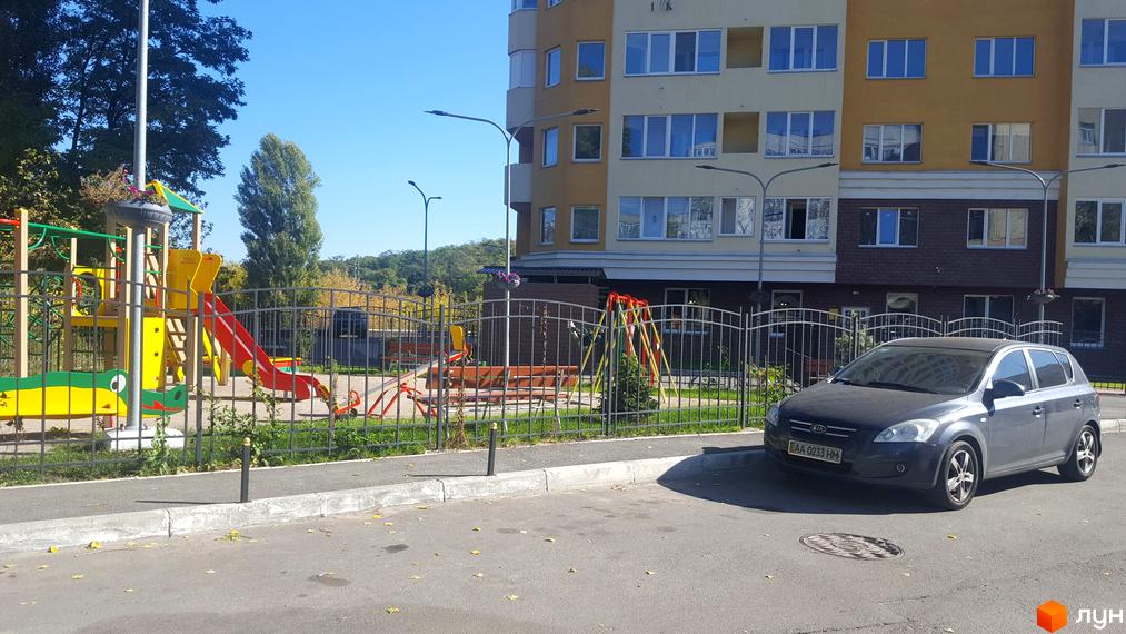 Багатоповерховий будинок ЖК Solo Park з великими вікнами. На прибудинковій території дитячий майданчик та парковка для автомобілів.