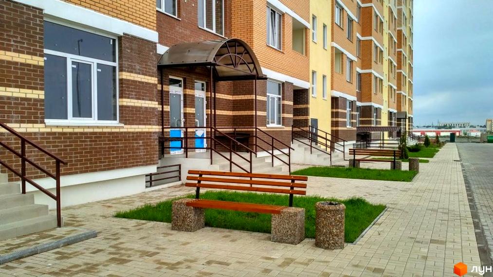 Зовнішній вигляд новобудови ЖК Цветной бульвар у Чорноморську. Прибудинкова територія з лавкою та доріжками з плитки.