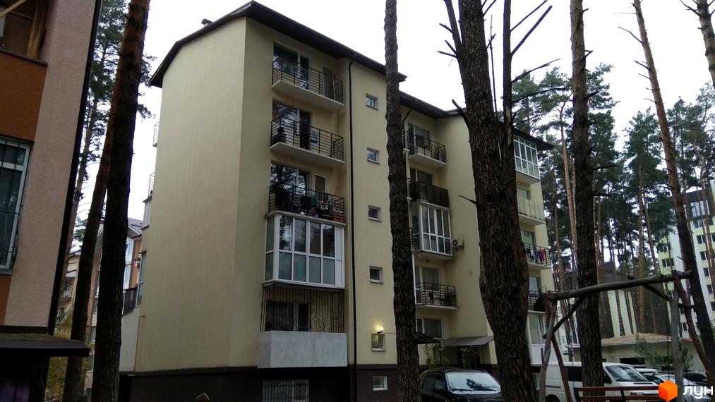 Клубний будинок „10-а лінія“ з балконами та вікнами, оточений деревами. На прибудинковій території видно дитячий майданчик та автомобілі.