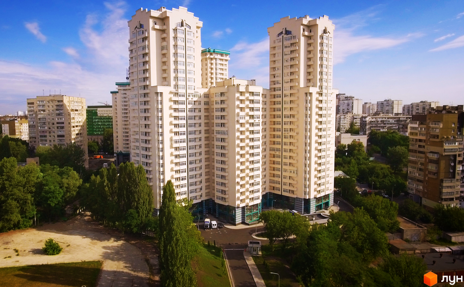 Висотки житлового комплексу Династія з великою кількістю вікон. На прибудинковій території багато зелені та є дорога для проїзду.