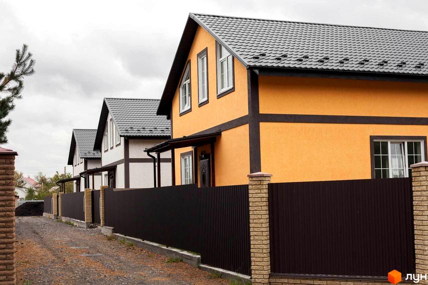 Котеджне містечко КМ Княжичі Хаус: двоповерхові будинки з помаранчевими та білими фасадами, темними дахами та парканами.