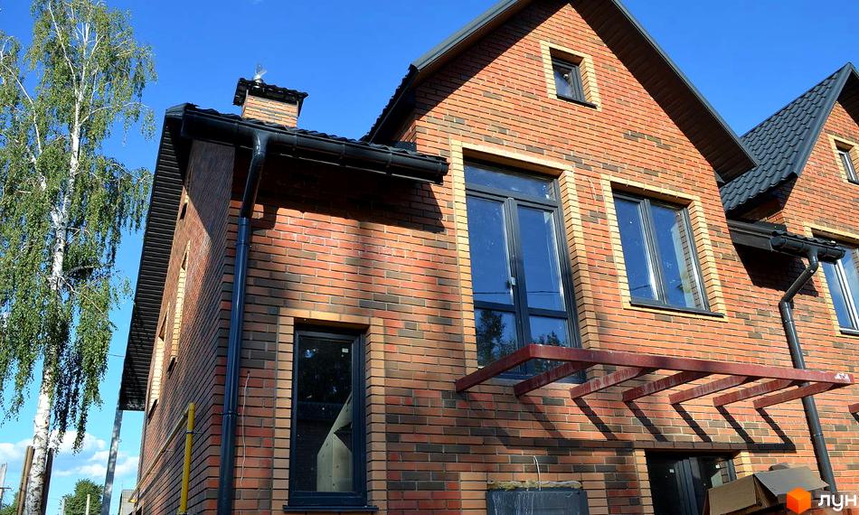 Таунхауси „На Вериківського“: цегляний фасад будинку з великими вікнами та чорним дахом. Поруч росте високе дерево.