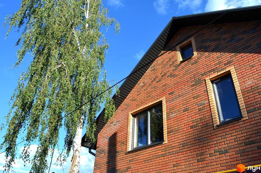 Таунхауси „На Вериківського“: цегляний будинок з вікнами та зелене дерево на фоні блакитного неба.