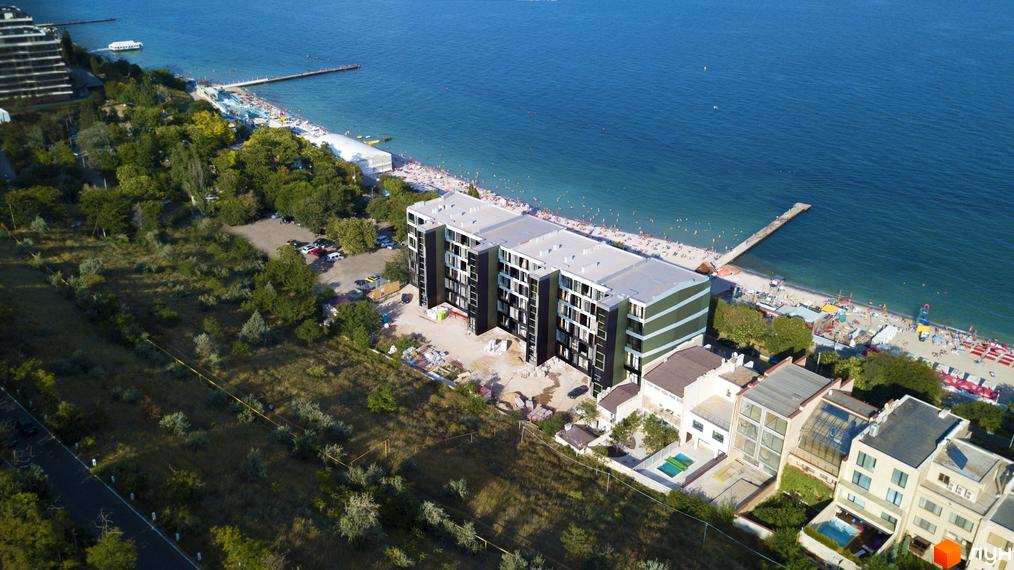 Житловий комплекс MAGNÍT. Будинок на Фонтані з фасадом з темних та зелених панелей, розташований біля моря та пляжу з відпочиваючими. Навколо комплексу зелена територія та прибудинкова забудова.