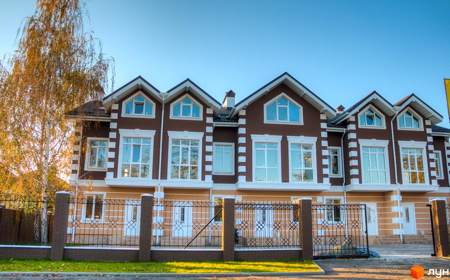 Зображення таунхаусів «Лісовий Маєток» з коричневими фасадами та великими вікнами. Перед будинками – металева огорожа та зелений газон.