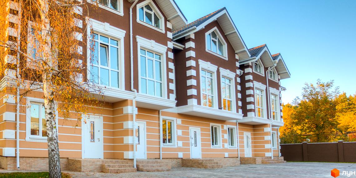 Ряд таунхаусів „Лісовий Маєток“ з коричнево-бежевим фасадом, білими вікнами та дверима. Навколо будівель вимощена територія та осінні дерева.