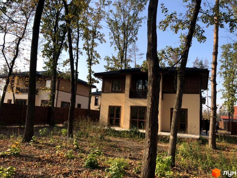 Котеджне містечко Віта Паркова: двоповерхові будинки з коричневими елементами фасаду, розташовані серед дерев. Навколо будинків - прибудинкова територія з опалим листям та травою.