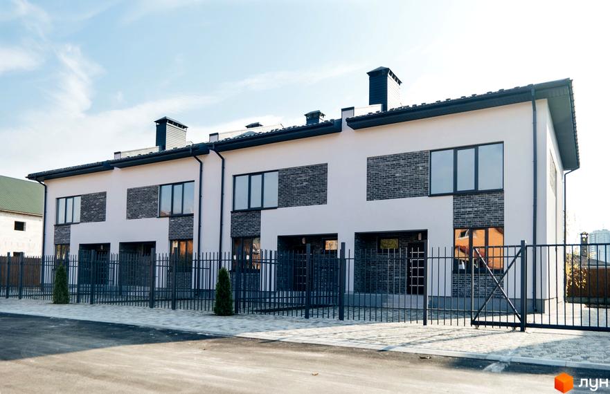 Таунхауси „На Підлісній“: двоповерхові будинки з білою штукатуркою та сірою цеглою, огороджені металевим парканом. Поруч розташована бруківка та зелені насадження.