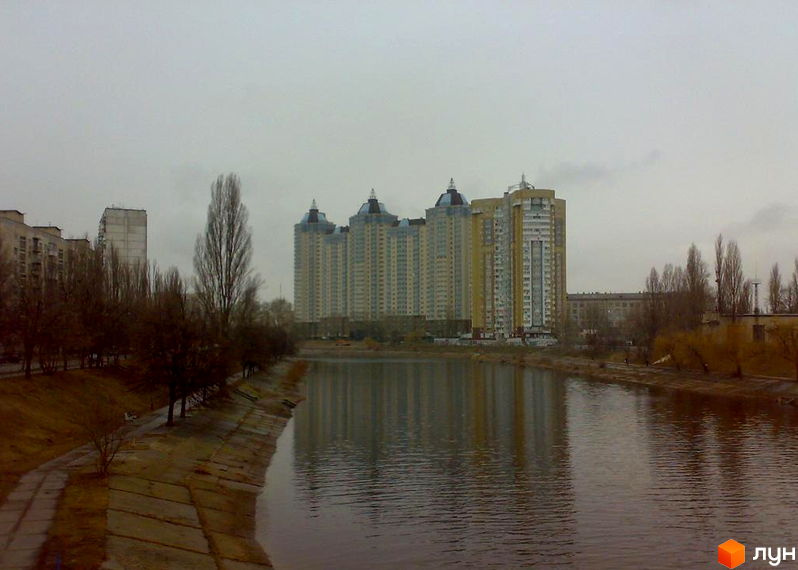 Житловий комплекс Лазурний блюз з висотними будинками біля водойми та прибудинковою територією з деревами.